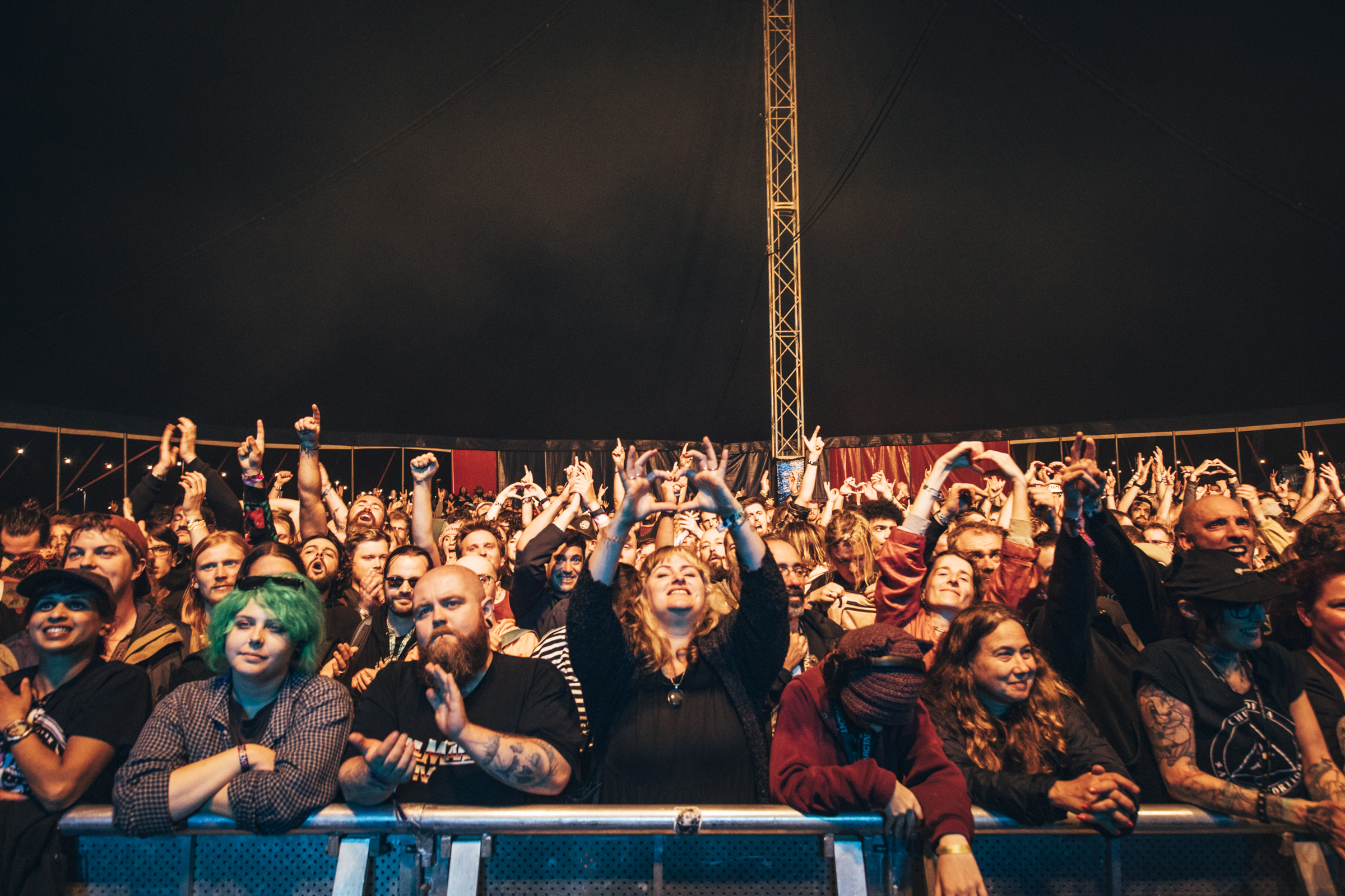 Crowd during and so i watch you from afar at ArcTanGent 2024, a lot of people holding their hands up in heart shapes above their heads.